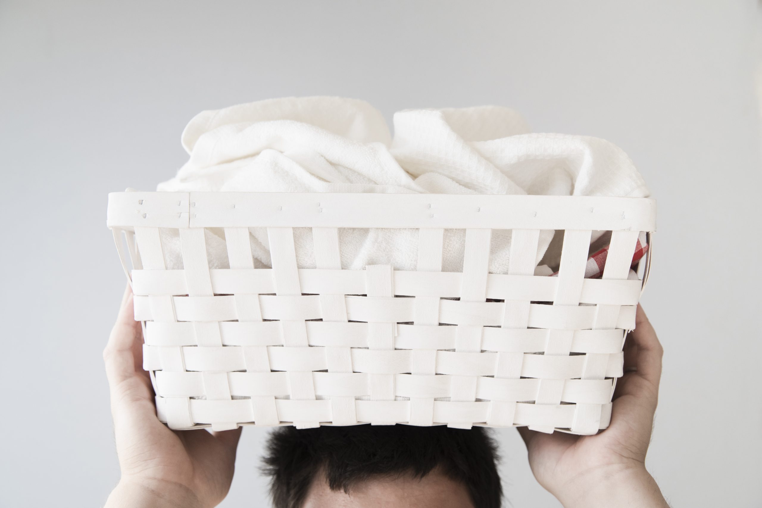 Mujer sosteniendo una cesta con productos de limpieza sobre fondo de color